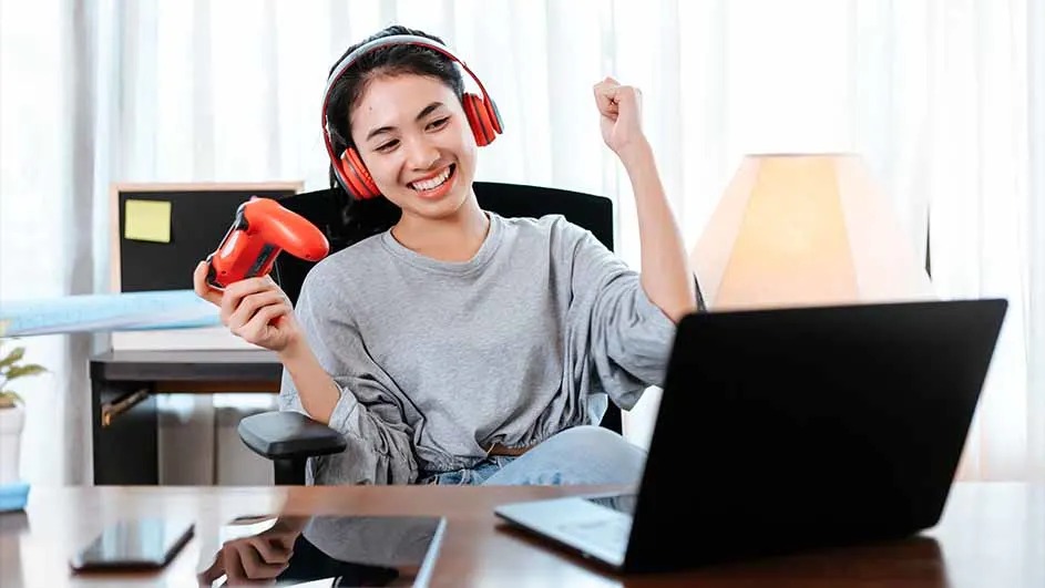 Une personne assise à un bureau avec un ordinateur portable, un casque rouge et une manette de jeu rouge.