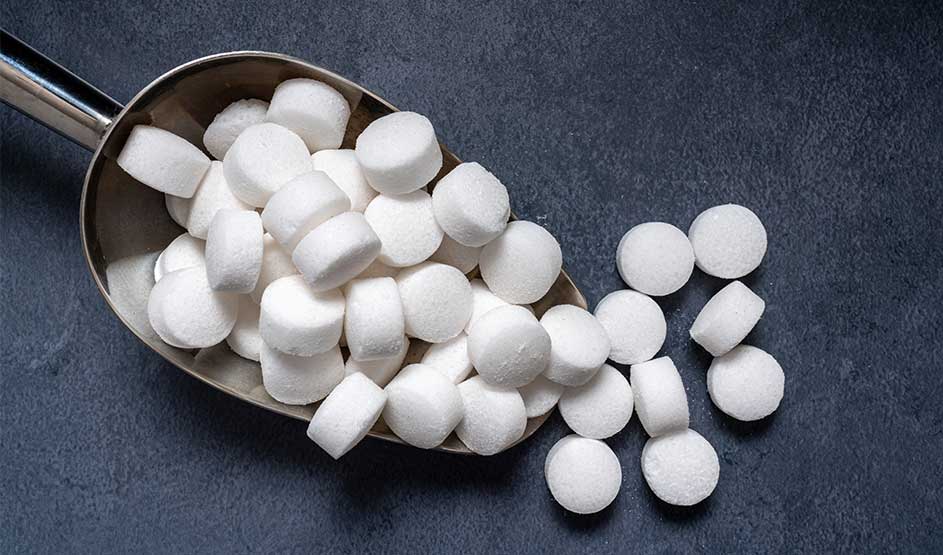 Pelle métallique sur fond sombre, remplie de petites pastilles blanches rondes; quelques-unes se sont répandues autour.