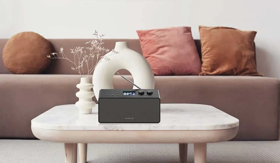 Radio noire sur une table basse en marbre, avec un canapé, des coussins et des vases en arrière-plan.