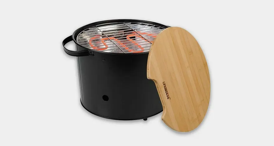A black electric grill sits beside a light wooden lid on a white surface.
