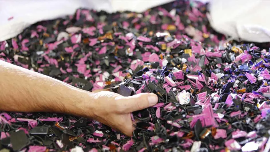 Une main dans un tas de plastique noir et rose. Le plastique est dans un sac blanc.