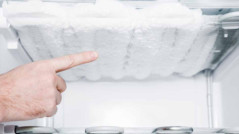 Intérieur de réfrigérateur blanc avec givre épais au plafond et une main pointant vers le givre.