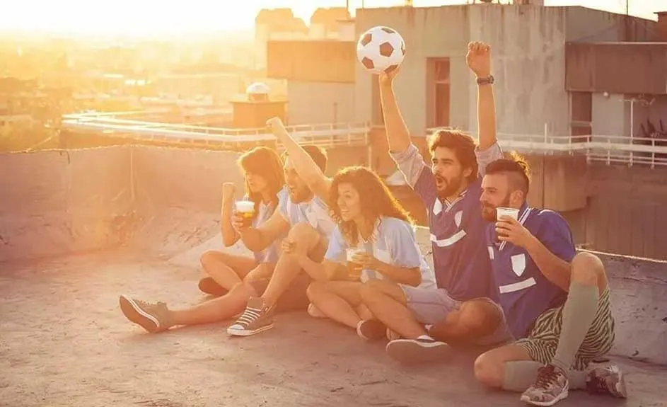 Un groupe est assis sur un toit-terrasse avec un ballon de football. Des bâtiments sont visibles à l'arrière-plan.