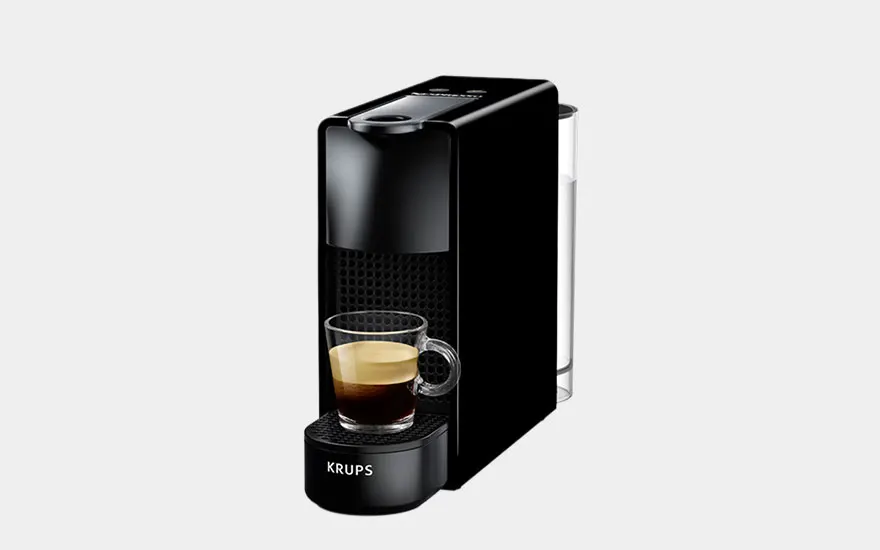 Een zwarte koffiemachine op een aanrecht met witte tegels en glazen potten met koffiecapsules.