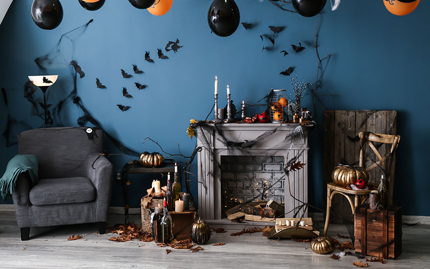 Een kamer is versierd voor Halloween met ballonnen, vleermuizen aan de muur en een beklede stoel naast een open haard.