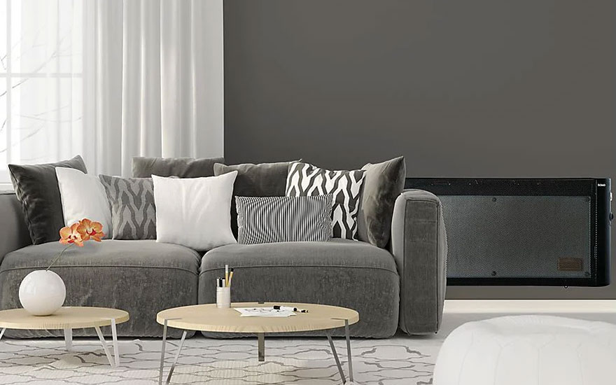 Een grijze sofa met kussens staat in een kamer met grijze muren, witte gordijnen en een zwart apparaat. Er zijn ronde tafels met voorwerpen.