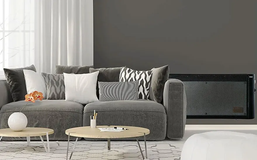 Een grijze sofa met kussens staat in een kamer met grijze muren, witte gordijnen en een zwart apparaat. Er zijn ronde tafels met voorwerpen.