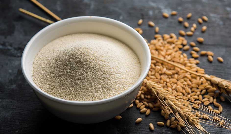 Un bol blanc rempli de semoule claire, accompagné d'épis de blé et de grains sur fond sombre.