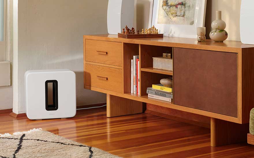 Meuble en bois avec livres, jeu d'échecs et vase. Un haut-parleur blanc est visible sur le sol en bois.