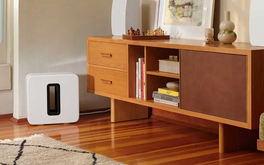 Een woonkamer met een houten kast, boeken, een wit apparaat en een schaakbord tegen een beige muur.