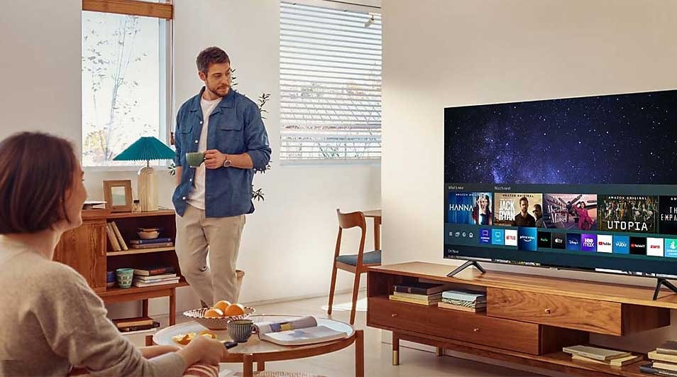Living room with a TV on a wooden stand showing streaming services, a bookshelf, and a round table.