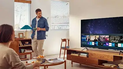 Living room with a TV on a wooden stand showing streaming services, a bookshelf, and a round table.