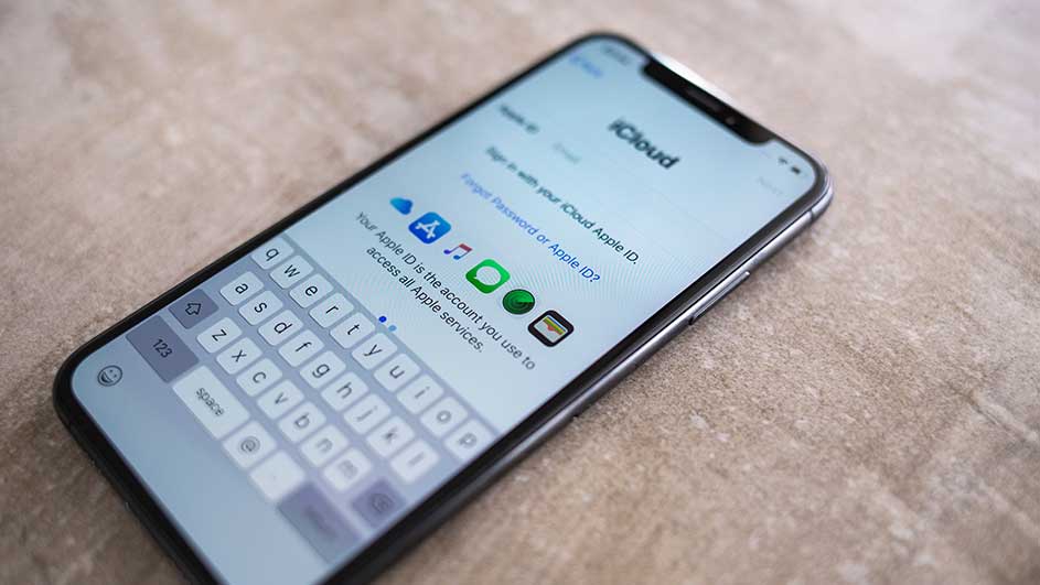Un iPhone affiche l'écran iCloud avec un clavier. Des icônes d'applications Apple sont visibles sur l'écran. Le fond est beige.