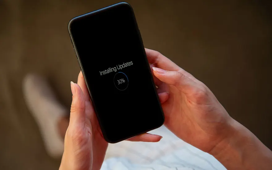 Een zwarte smartphone, vastgehouden door twee handen, geeft 'Updates installeren' weer met 30% voltooid. Vage achtergrond.
