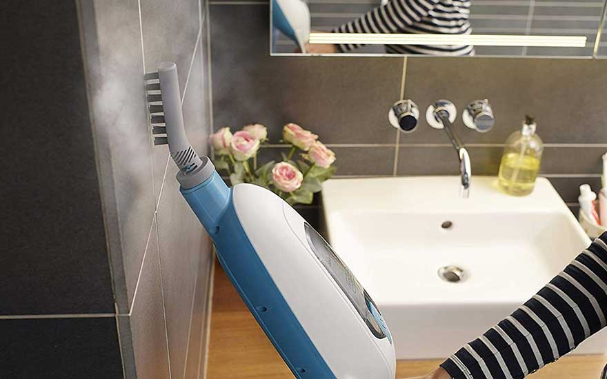 Een blauw-witte stoomreiniger maakt tegels schoon in een badkamer met een wastafel en roze bloemen.