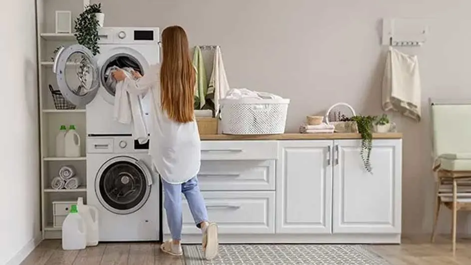 Buanderie avec lave-linge blanc, armoires, panier à linge et produits de nettoyage.