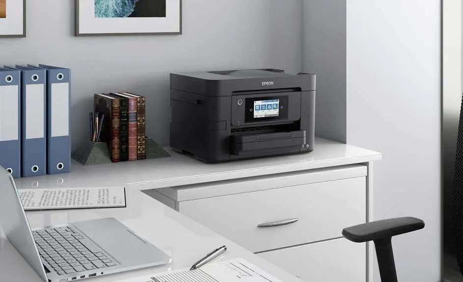 Bureau met een printer, laptop, ringmappen, boeken, een pen en documenten in een nette kantooromgeving.