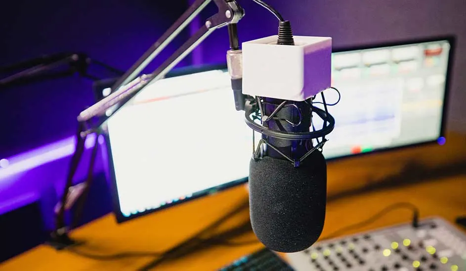 Micro noir sur pied réglable, écran PC allumé, clavier gris sur bureau bois, ambiance violette.