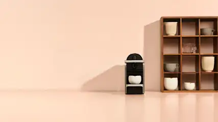 Coin café minimaliste avec une machine compacte et des tasses dans une étagère à cases en bois.