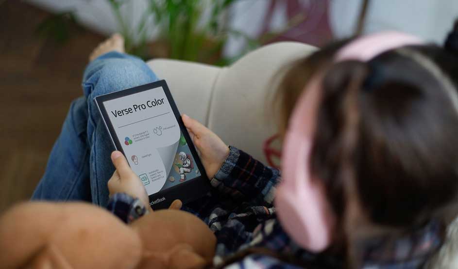 A person holds an e-reader displaying "Verse Pro Color". Plants and home decor visible in background. Cozy, rustic home atmosphere with focus on digital reading.