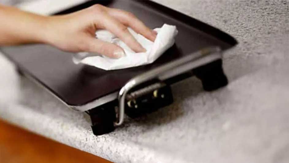 Main nettoyant une plaque de cuisson noire avec un chiffon blanc sur un comptoir moucheté.