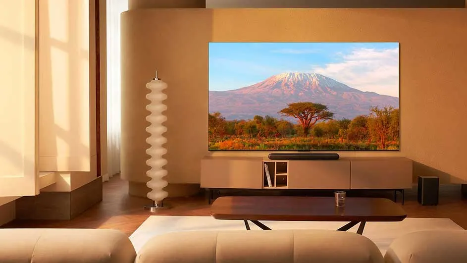 Salon beige avec un téléviseur affichant une montagne et des arbres, une table basse et un lampadaire.