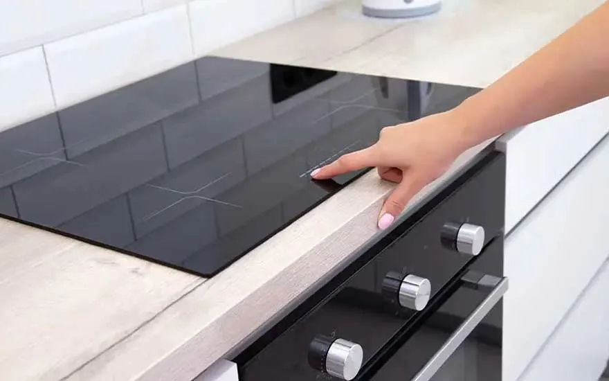 Een zwarte kookplaat bevindt zich op een lichtkleurig aanrecht, met een hand die de kookplaat aanraakt. Een zwarte oven is zichtbaar.