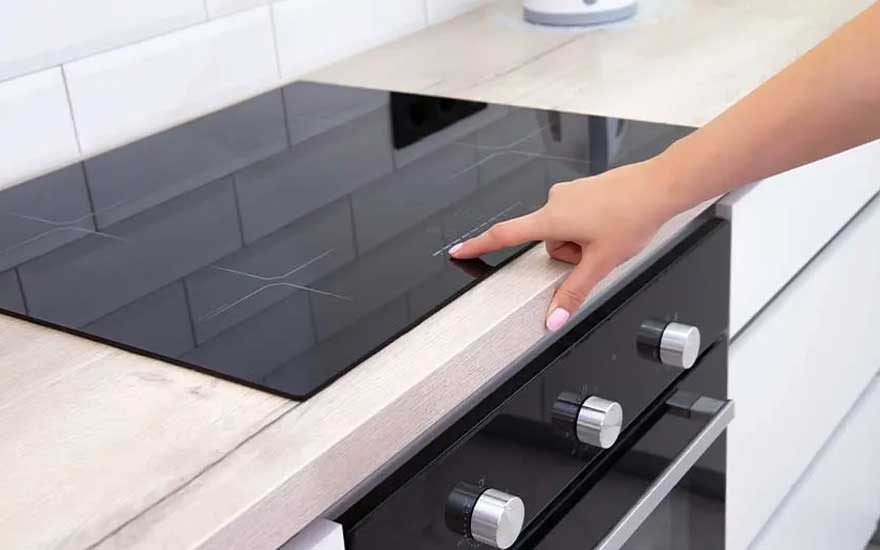 Een zwarte kookplaat bevindt zich op een lichtkleurig aanrecht, met een hand die de kookplaat aanraakt. Een zwarte oven is zichtbaar.