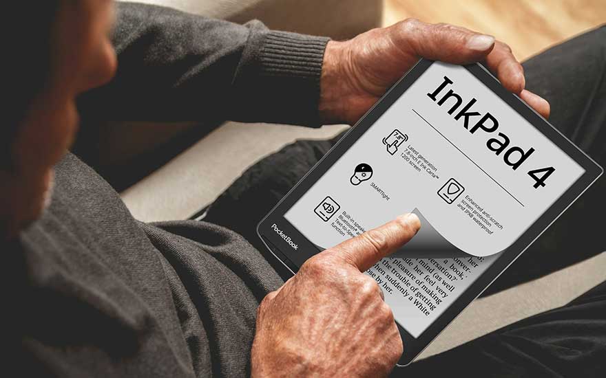 Un homme tient une liseuse InkPad 4. L'écran affiche des informations et du texte. Il est assis sur un canapé gris.