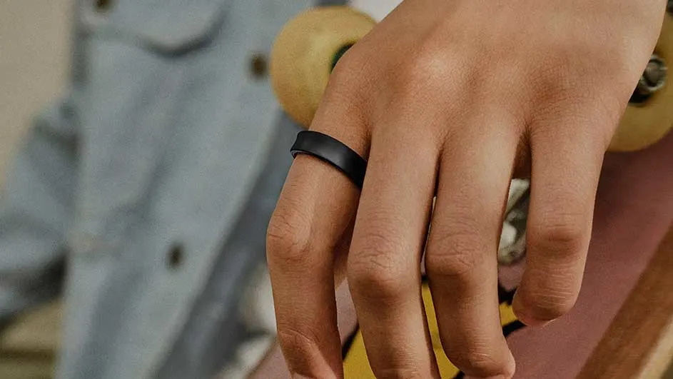 Main tenant une planche à roulettes, une main porte une bague noire. Le fond est un vêtement bleu.