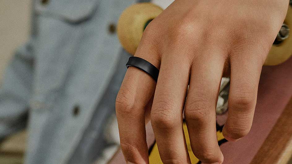 Een hand met een zwarte ring om een vinger, op de achtergrond een skateboard met gele wielen.