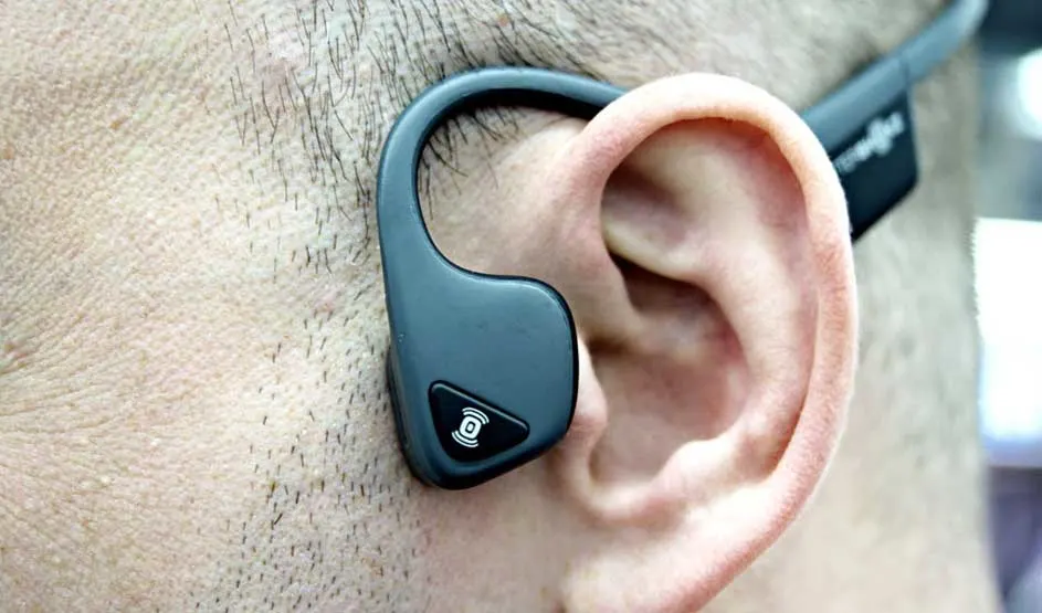 Een close-up toont een grijs beengeleidingshoofdtelefoon die over een oor haakt.