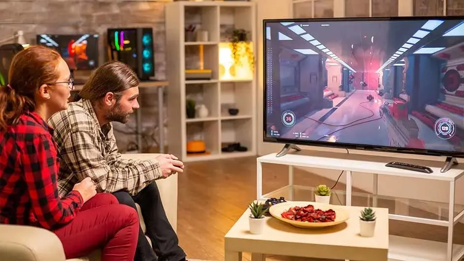 Woonkamer met tv met een videospel, witte kast, snack op tafel en decoratieve planten.