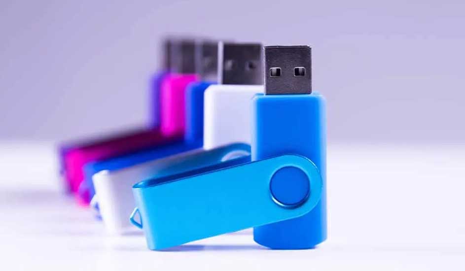 Rangée de clés USB colorées (bleu, blanc, rose) sur fond clair. Les connecteurs USB sont métalliques.