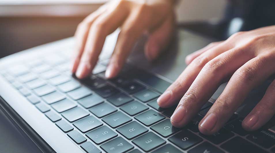 Gros plan sur un clavier d'ordinateur portable gris avec des mains tapant. L'éclairage est doux et directionnel.