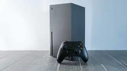 Een zwarte spelconsole met een strak ontwerp staat rechtop, vergezeld door een zwarte controller, tegen een lichte achtergrond.