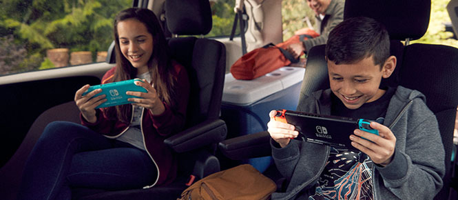 Twee kinderen zitten in een auto en spelen op een Nintendo Switch. Op de achtergrond een koelbox en een tas.