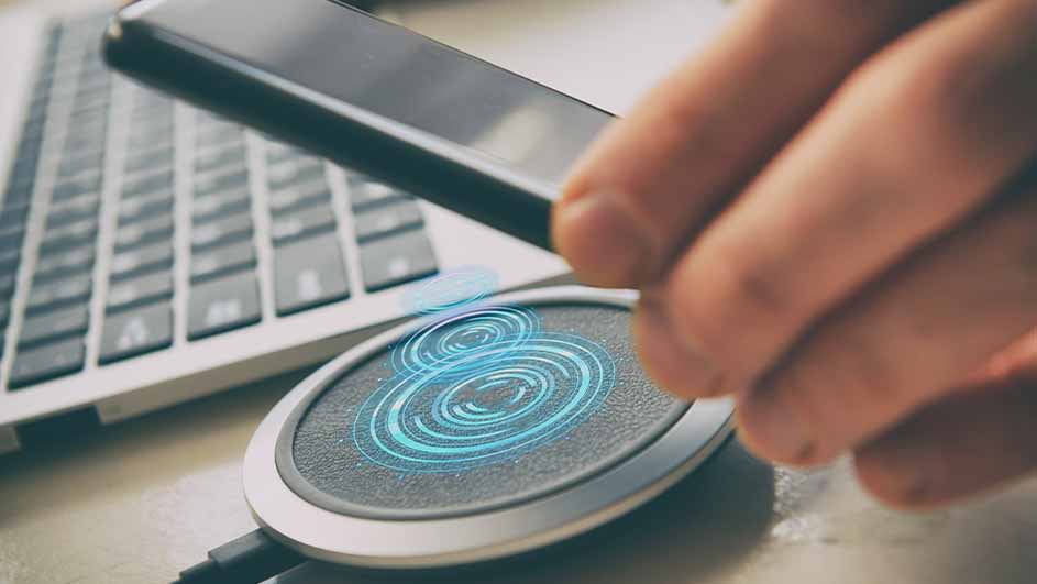 Un smartphone est placé au-dessus d'un chargeur sans fil rond avec des cercles lumineux bleus, à côté d'un clavier d'ordinateur.