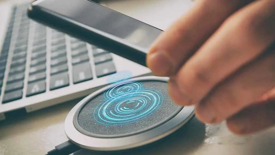 Un smartphone est placé au-dessus d'un chargeur sans fil rond avec des cercles lumineux bleus, à côté d'un clavier d'ordinateur.