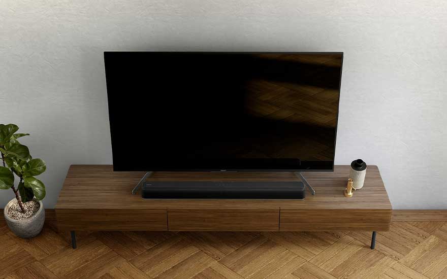 Un téléviseur noir sur un meuble TV brun avec une plante en pot et une bouteille blanche sur un parquet en bois.