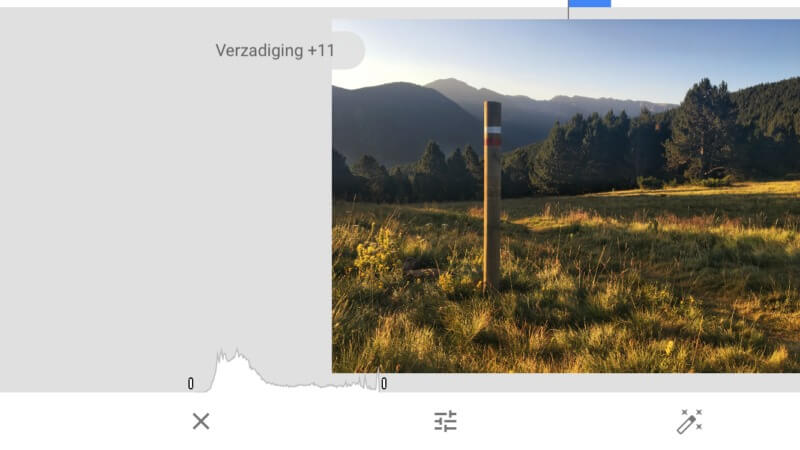Een landschap met een houten paal in een veld. Op de achtergrond zijn bergen en bomen zichtbaar onder een blauwe hemel.