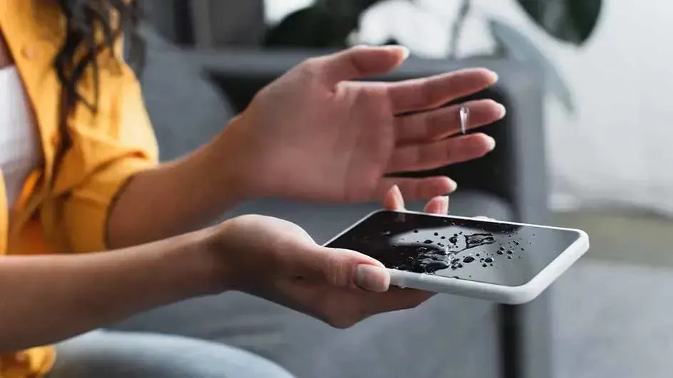 Een hand veegt waterdruppels van het scherm van een zwarte smartphone met witte rand, merk is niet zichtbaar.