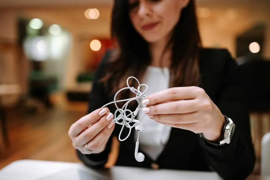 Gros plan sur des écouteurs blancs emmêlés tenus par deux mains, avec un arrière-plan flou.