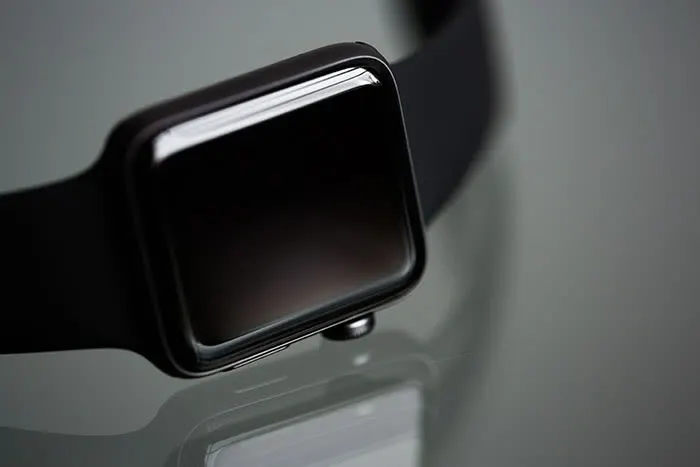 Een zwarte smartwatch met een vierkant scherm en een band ligt op een gladde, grijze ondergrond.