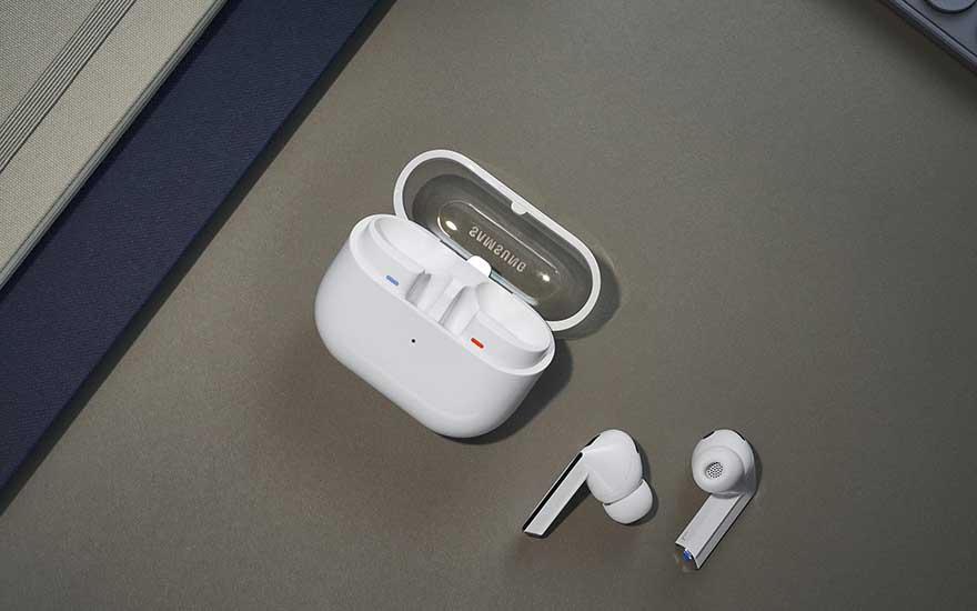 Des écouteurs sans fil blancs sont posés près d’un boîtier de charge ouvert avec logo Samsung, sur une surface grise à bord bleu.