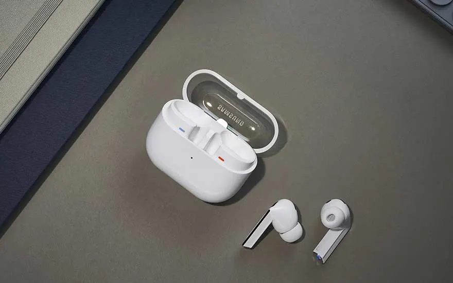 Witte draadloze oordopjes liggen naast een open oplaadcase met Samsung-logo, op een grijs oppervlak met een donkerblauwe rand.