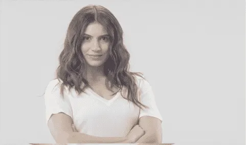 Une personne porte un t-shirt blanc à manches courtes sur un fond blanc uni. Les bras sont croisés.