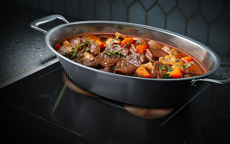 Ragoût de bœuf dans une casserole ovale en métal sur une plaque de cuisson noire avec des légumes colorés.