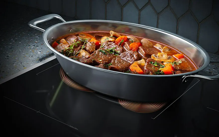 Ragoût de bœuf dans une casserole ovale en métal sur une plaque de cuisson noire avec des légumes colorés.