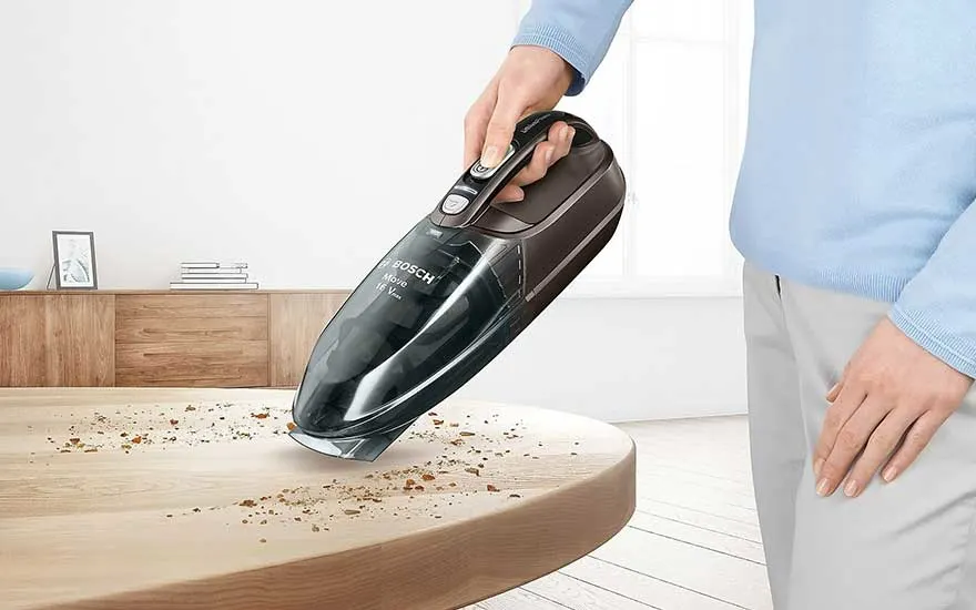 Een kruimeldief van Bosch zuigt kruimels op van een houten tafel. Op de achtergrond staat een houten kast.